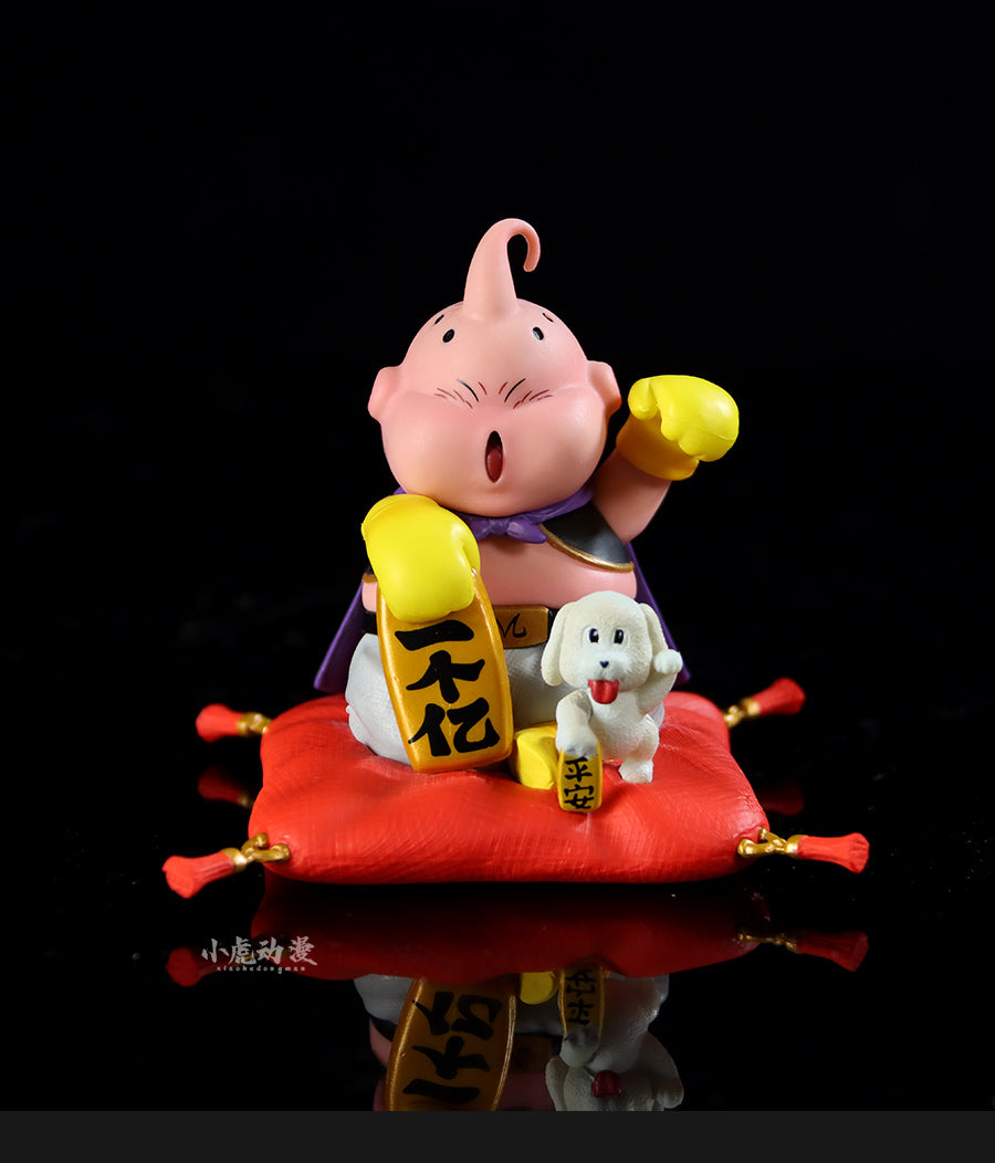 The Seakoff Majin Buu Collectible Figure is an 8.5cm Dragon Ball Z statue featuring the pink character with a single antenna and yellow gloves, sitting on a red cushion, holding a yellow object with black markings. A small white dog rests beside it against a black background. Lucky New Year Edition.