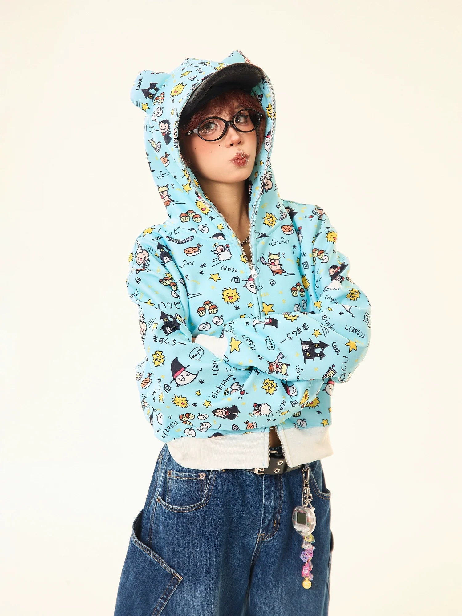 Against a plain background, a person in Seakoff's Kawaii Cartoon Bear Hoodie—featuring cute ears and fun prints—exudes whimsical streetwear style. Completing the look with crossed arms, they pair it with loose-fitting jeans embellished with quirky accessories.