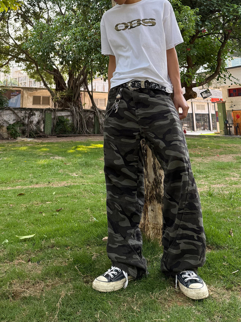 Pantalon cargo camouflage foncé à jambes larges, finition vintage délavée, porté avec un t-shirt court et des bottines noires