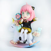 This 15 cm Anya Forger PVC figure from Spy × Family features a cheerful chibi-style design with interchangeable face expressions, sitting on a pastel unicorn. Adorned in a black and gold outfit, pink hair, and green eyes, it includes a plush with a blue face on the unicorn&