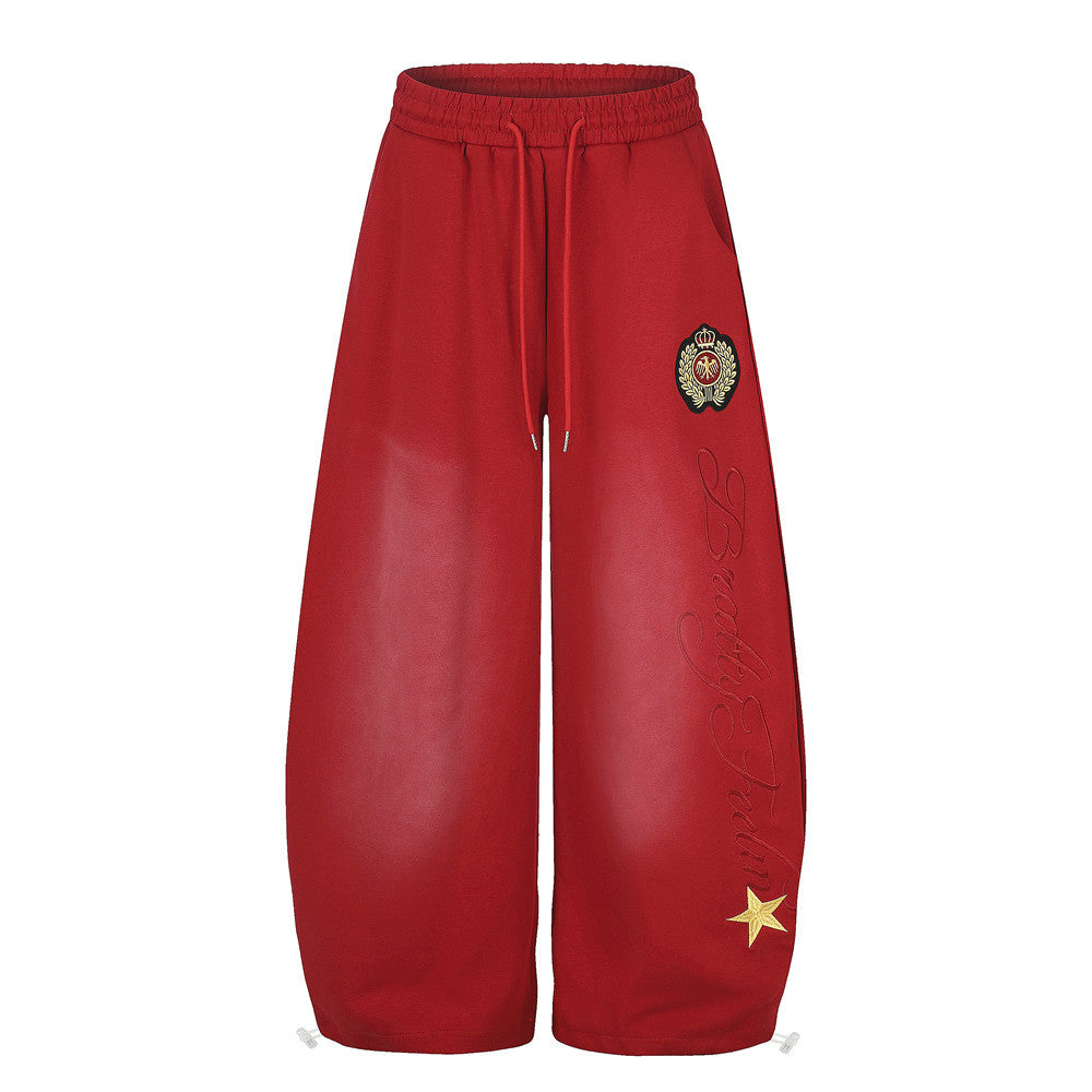 Men's oversized wide-leg sweatpants in red with cursive script embroidery, woven crest badge, and gold star appliqué
