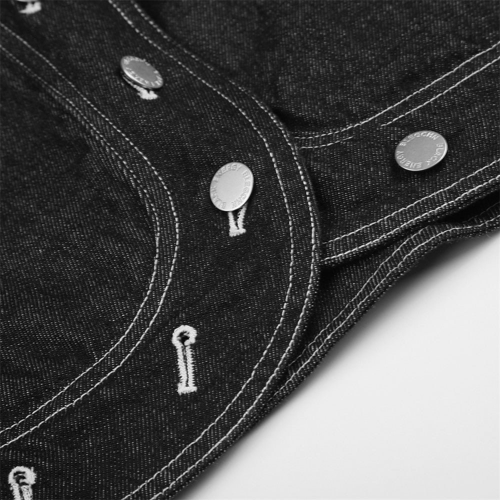 Close-up of black denim jacket hem with curved stitching and snap details