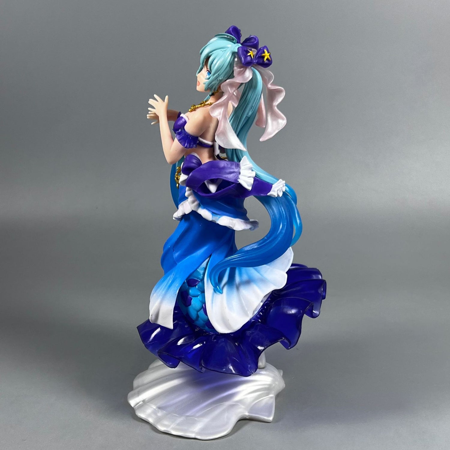 The Hatsune Miku Mermaid 24cm PVC Figure features blue-haired character Hatsune Miku in a detailed mermaid-inspired outfit in shades of blue, purple, and white, complete with a star accessory and ruffled dress design—an elegant collectible for Vocaloid fans.