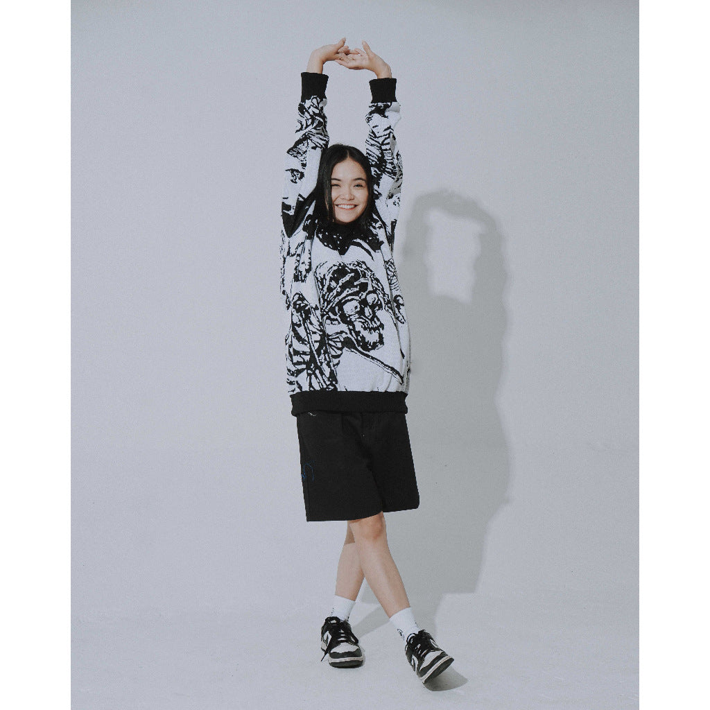 A person poses with arms raised, wearing Seakoff's Premium Skeleton Warrior Knit Sweater—a gothic jacquard design—paired with black shorts, sneakers, and white socks. Their shadow is cast on the light gray wall, enhancing the ensemble's gothic streetwear vibe.