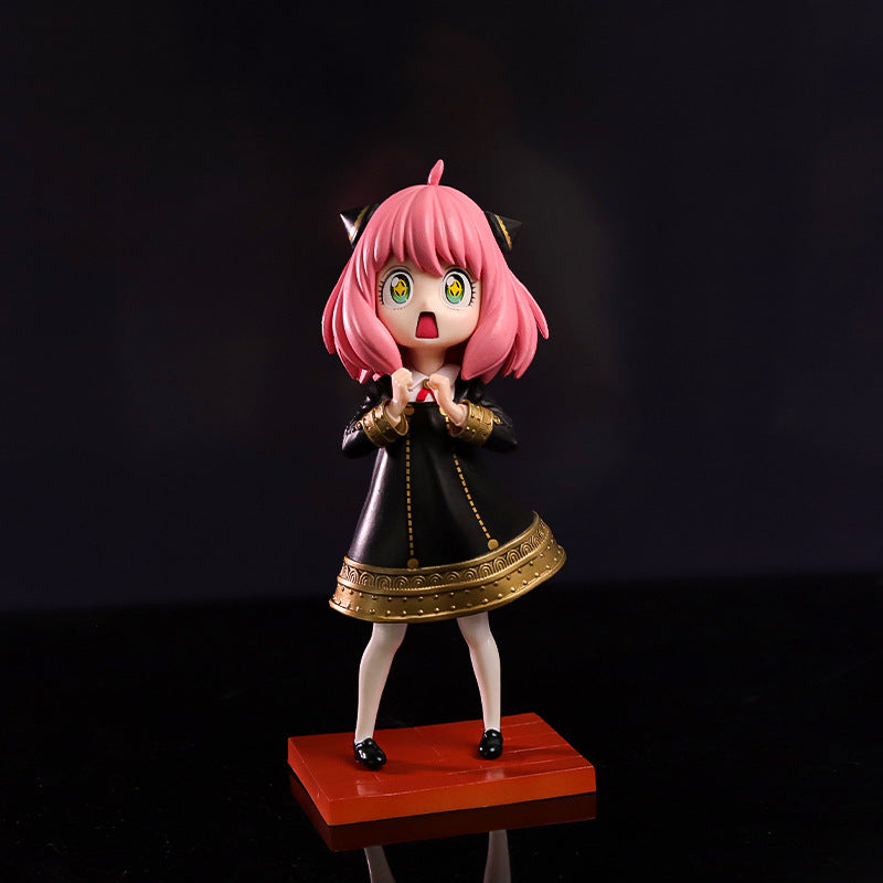 The Spy × Family Anya Forger PVC Figure, 17 cm tall, features Anya with her signature starry eyes expression. She stands on an orange base, adorned in a black dress with gold trim and pink hair styled with cat ear-like accessories, while wearing white socks and black shoes.