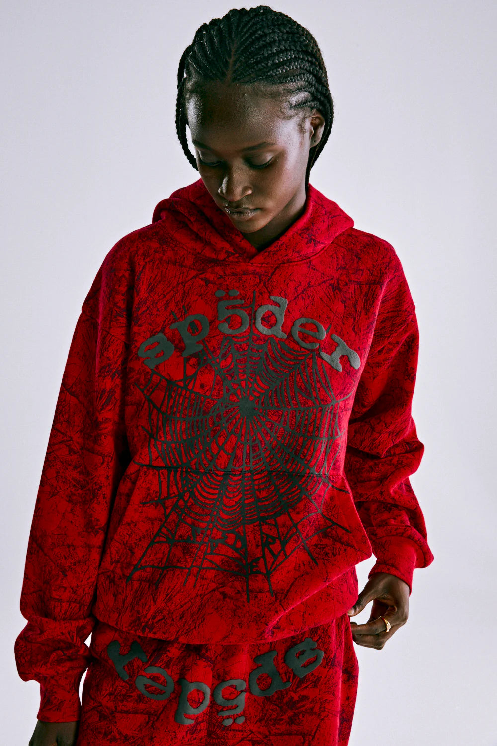 Wearing the Red Sp5der Web Hoodie 440GSM – Red Spider Web Graphic Hoodie and matching pants with black spiderwebs and "spider" on the front, a person looks down with hands at their sides, bringing bold streetwear style.
