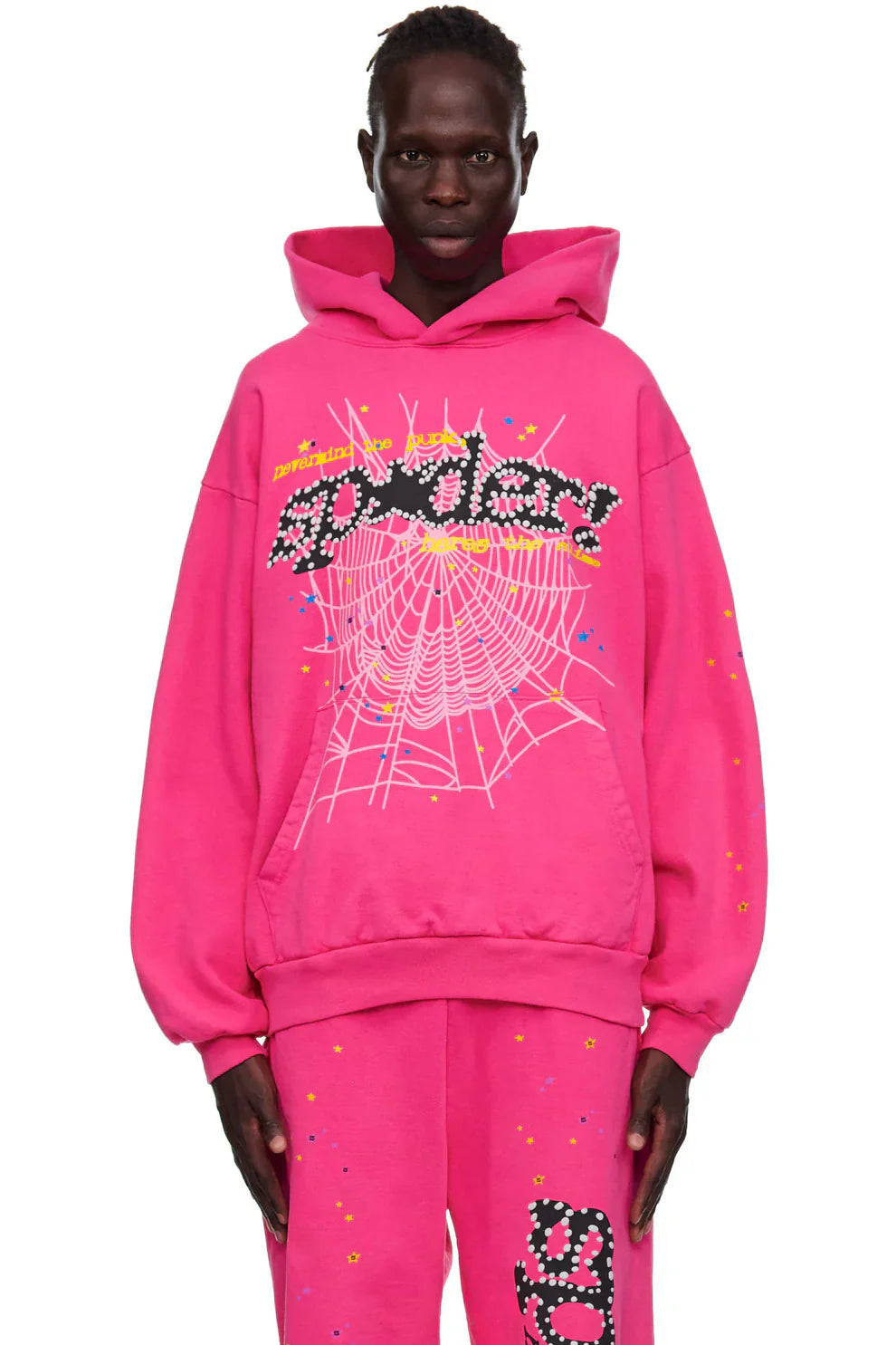 Wearing the Sp5der “Nevermind the Punk” Hot Pink Hoodie— a 440GSM heavyweight pullover with bold spiderwebs, So Class text, and paint splatter— this look channels punk streetwear vibes against a white background.