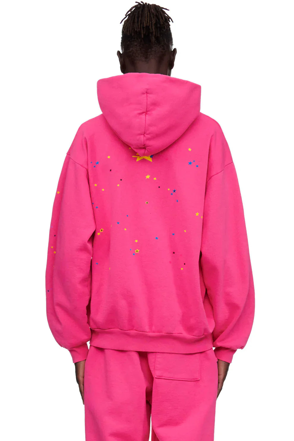 A person wearing the Sp5der “Nevermind the Punk” Hoodie – Hot Pink 440GSM Heavyweight Streetwear Pullover and matching pants, shown from the back. Colorful star and dot patterns decorate the upper back, bringing a bold Y2K punk streetwear vibe.