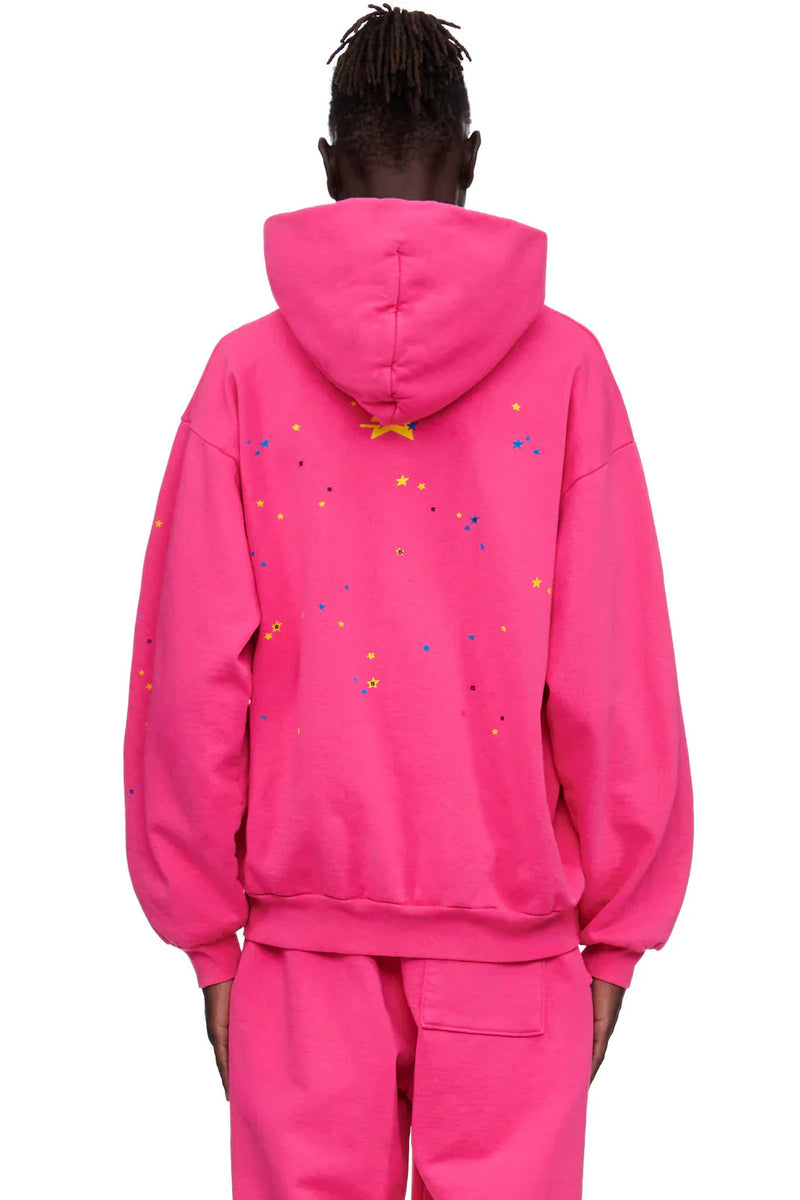 A person wearing the Sp5der “Nevermind the Punk” Hoodie – Hot Pink 440GSM Heavyweight Streetwear Pullover and matching pants, shown from the back. Colorful star and dot patterns decorate the upper back, bringing a bold Y2K punk streetwear vibe.