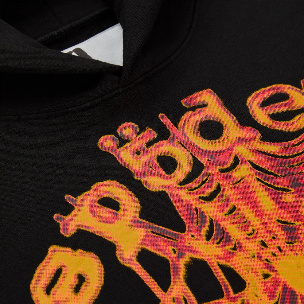 Close-up of the Sp5der Web Graphic Hoodie – Black & Orange 440GSM Heavyweight Streetwear, featuring a bold abstract graphic with "apple" in distorted yellow and orange lettering radiating outward, echoing the edgy style of a spider web design.