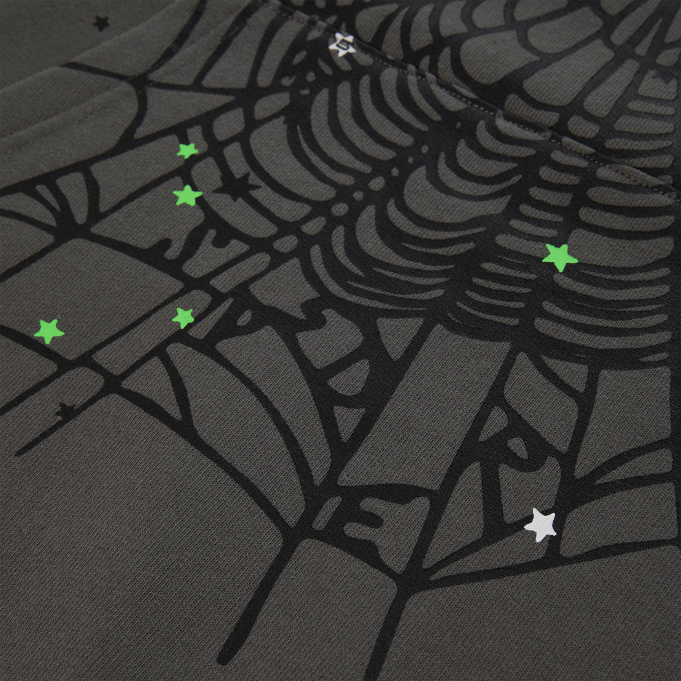 A close-up of heavyweight cotton fleece featuring the Sp5der “P!nk! Hares the Slime” Hoodie in olive green, a streetwear-inspired 440GSM pullover with a printed spiderweb and scattered small green and white star designs.
