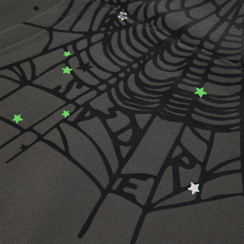 A close-up of heavyweight cotton fleece featuring the Sp5der “P!nk! Hares the Slime” Hoodie in olive green, a streetwear-inspired 440GSM pullover with a printed spiderweb and scattered small green and white star designs.