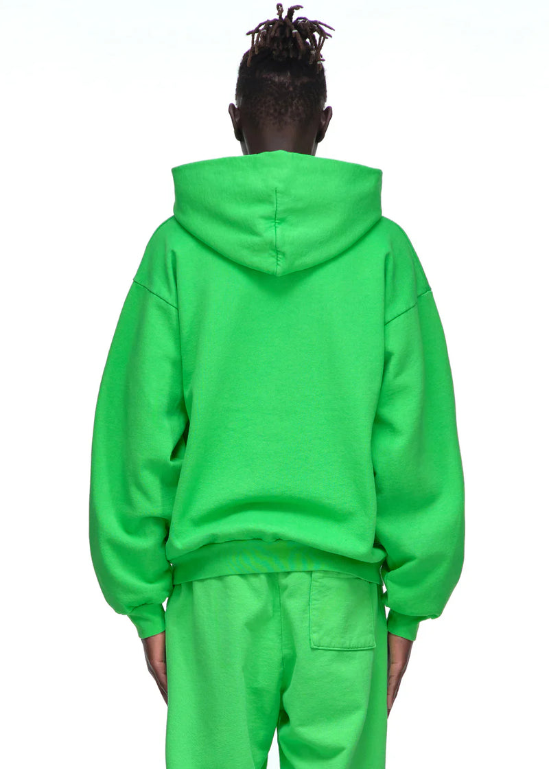A person with short dreadlocks is seen from behind, wearing a neon green Sp5der “Web Core” Hoodie—440GSM heavyweight oversized streetwear pullover—paired with matching sweatpants, both featuring one back pocket, against a plain white background.