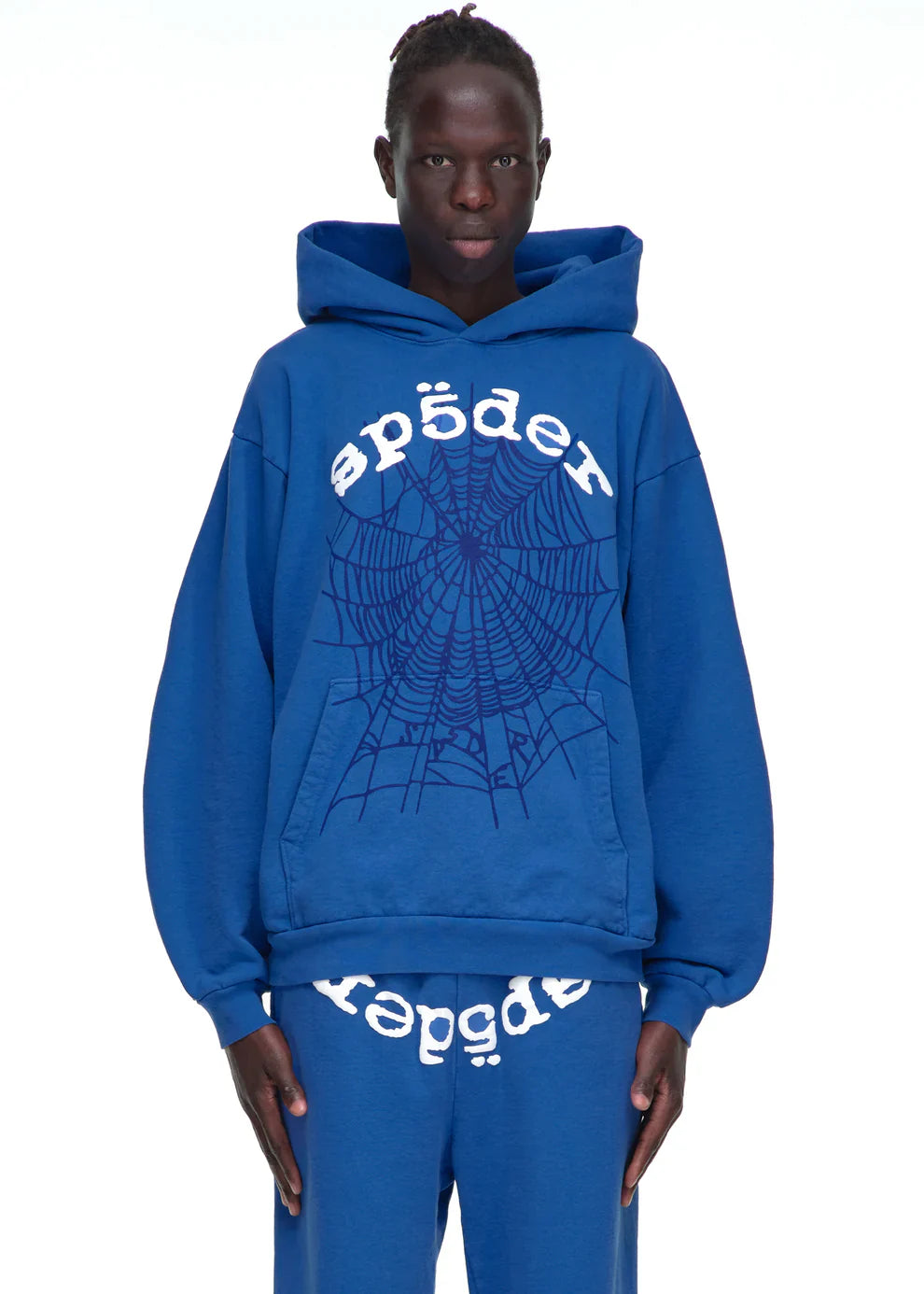 Wearing the Sp5der OG Web Hoodie 440GSM—a royal blue heavyweight cotton fleece sweatshirt with “sp5der” and a black spiderweb graphic—paired with matching sweatpants featuring upside-down text, shown on a plain white background.