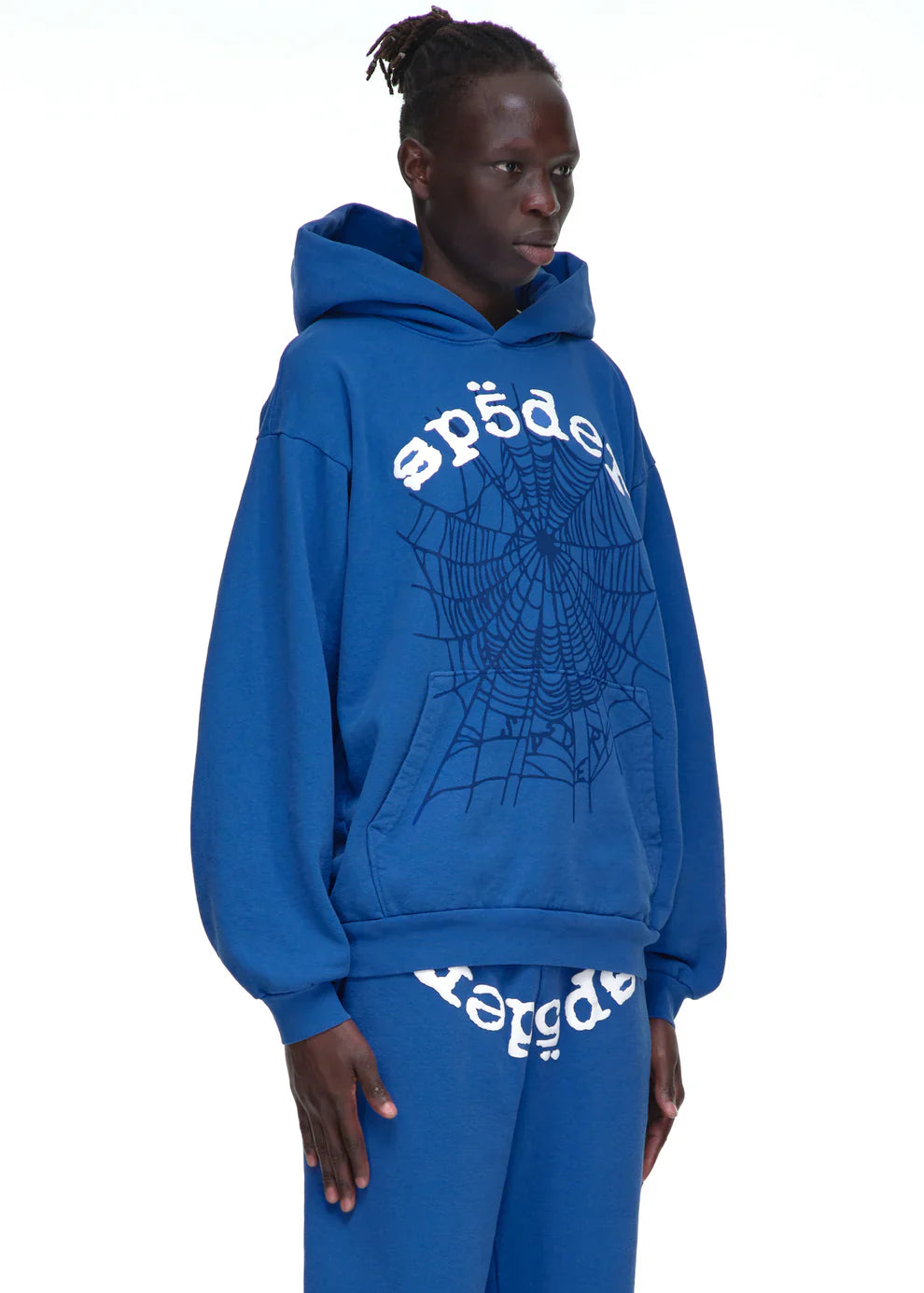 A person wearing the Sp5der OG Web Hoodie 440GSM – Royal Blue Heavyweight Spider-Web Graphic Sweatshirt with matching pants, featuring white Cyrillic text and a large spiderweb graphic, stands against a plain white background.