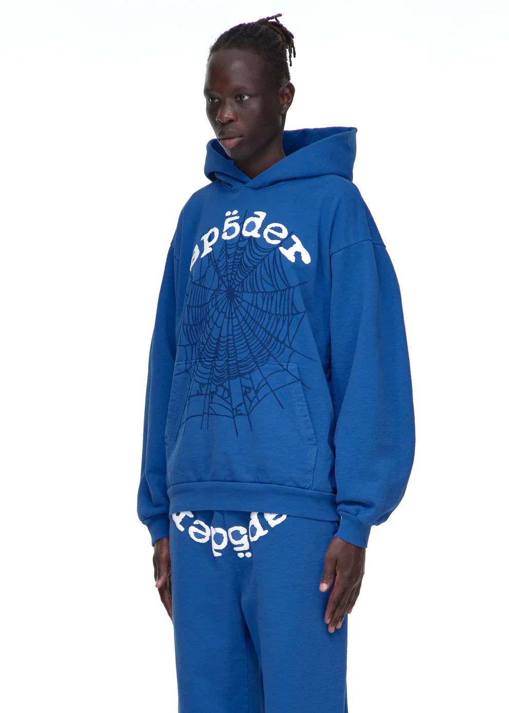 A person wears the Sp5der OG Web Hoodie 440GSM – Royal Blue Heavyweight Spider-Web Graphic Sweatshirt with matching blue sweatpants, standing against a plain white background.