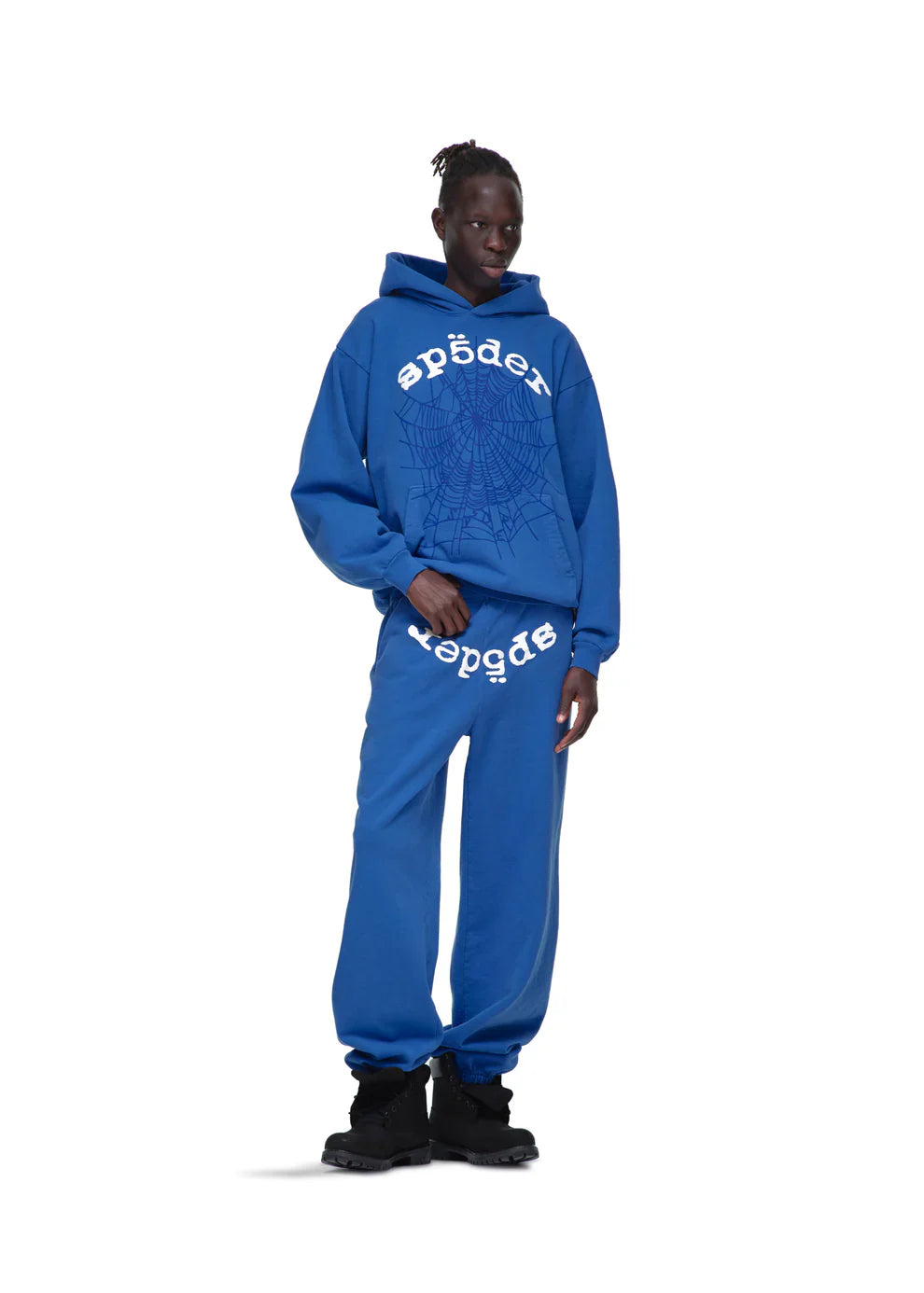 Wearing a Sp5der OG Web Hoodie 440GSM – Royal Blue Heavyweight Spider-Web Graphic Sweatshirt with matching blue sweatpants and black shoes, a person poses against a plain white background.