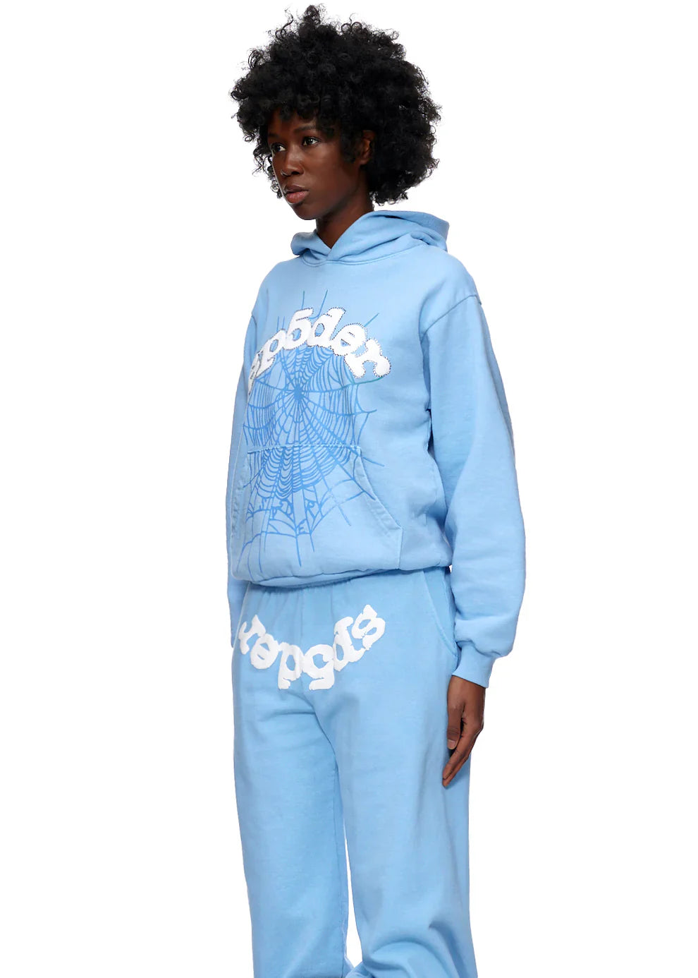 Wearing the Sp5der Hoodie – Sky Blue 440GSM Heavyweight Chenille Logo Spider-Web Pullover and matching sweatpants, a person stands against a white backdrop. The streetwear set showcases a white spiderweb graphic and bold text for standout style.