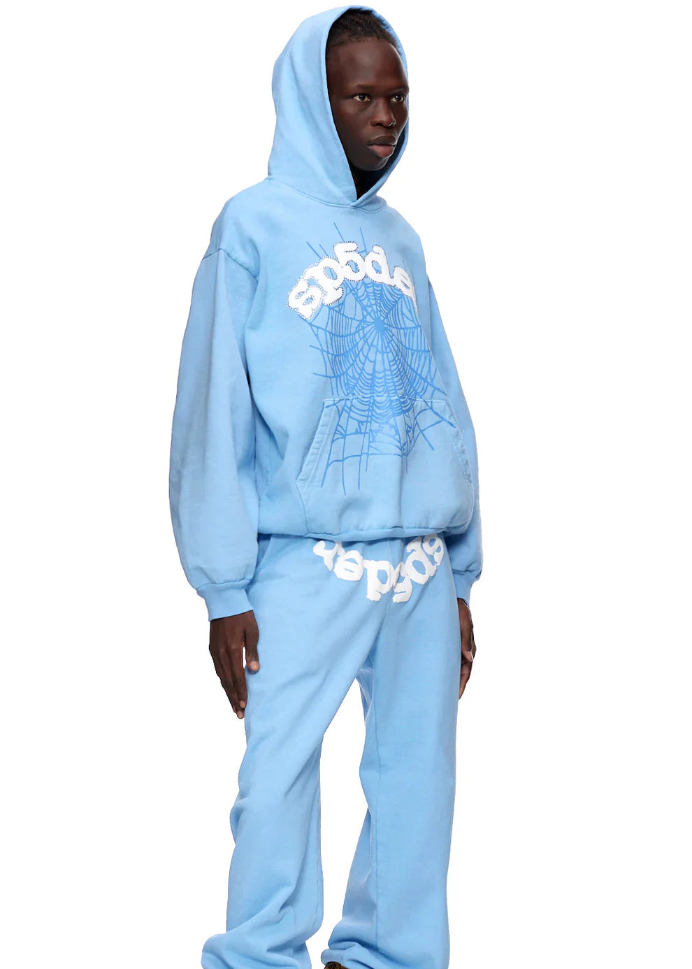 A person stands against a plain background wearing the Sp5der Hoodie – Sky Blue 440GSM Heavyweight Chenille Logo Spider-Web Streetwear Pullover with matching sweatpants, featuring white graphic text and spider web details, plus "sp5der" on the chest.
