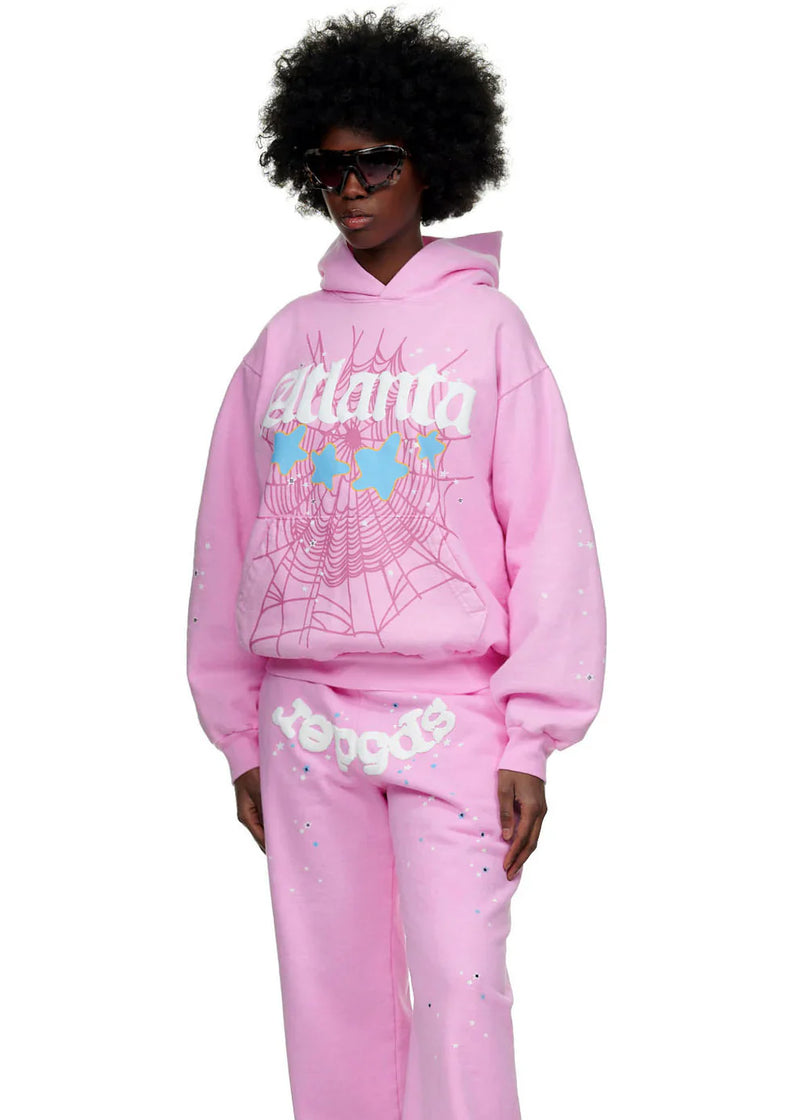 Wearing the Sp5der Atlanta Hoodie – Pink 440GSM Heavyweight Y2K Streetwear Pullover with matching sweatpants and bold shades, this look boasts white spiderweb prints, light blue details, and retro vibes for Y2K street style lovers.