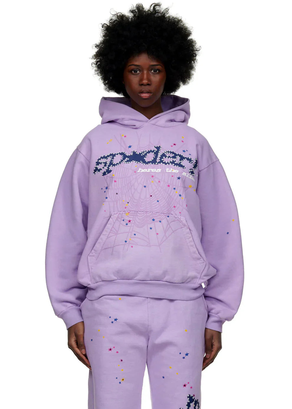 A person stands facing forward in the Sp5der “Hares the Slime” Hoodie – a lavender purple 440GSM heavyweight pullover with colorful splatter and spider-web graphics – for a bold streetwear look against a white background.