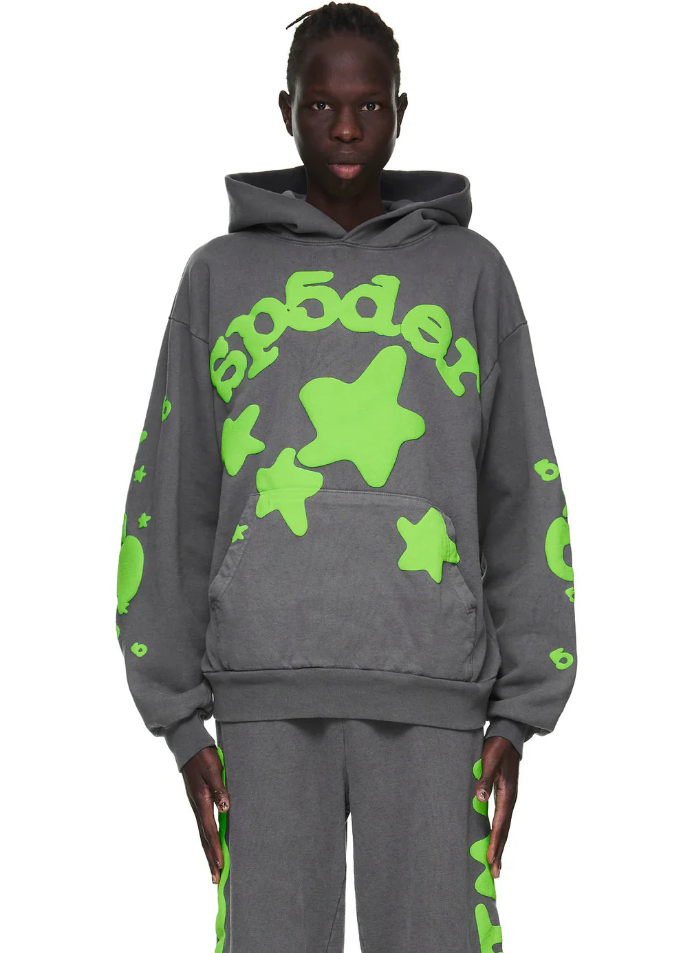 A person faces forward against a plain background, wearing the Green and Grey Sp5der Hoodie – a 440GSM heavyweight oversized sweatshirt with bright green star graphics and “sp5der” text, exuding bold streetwear style.