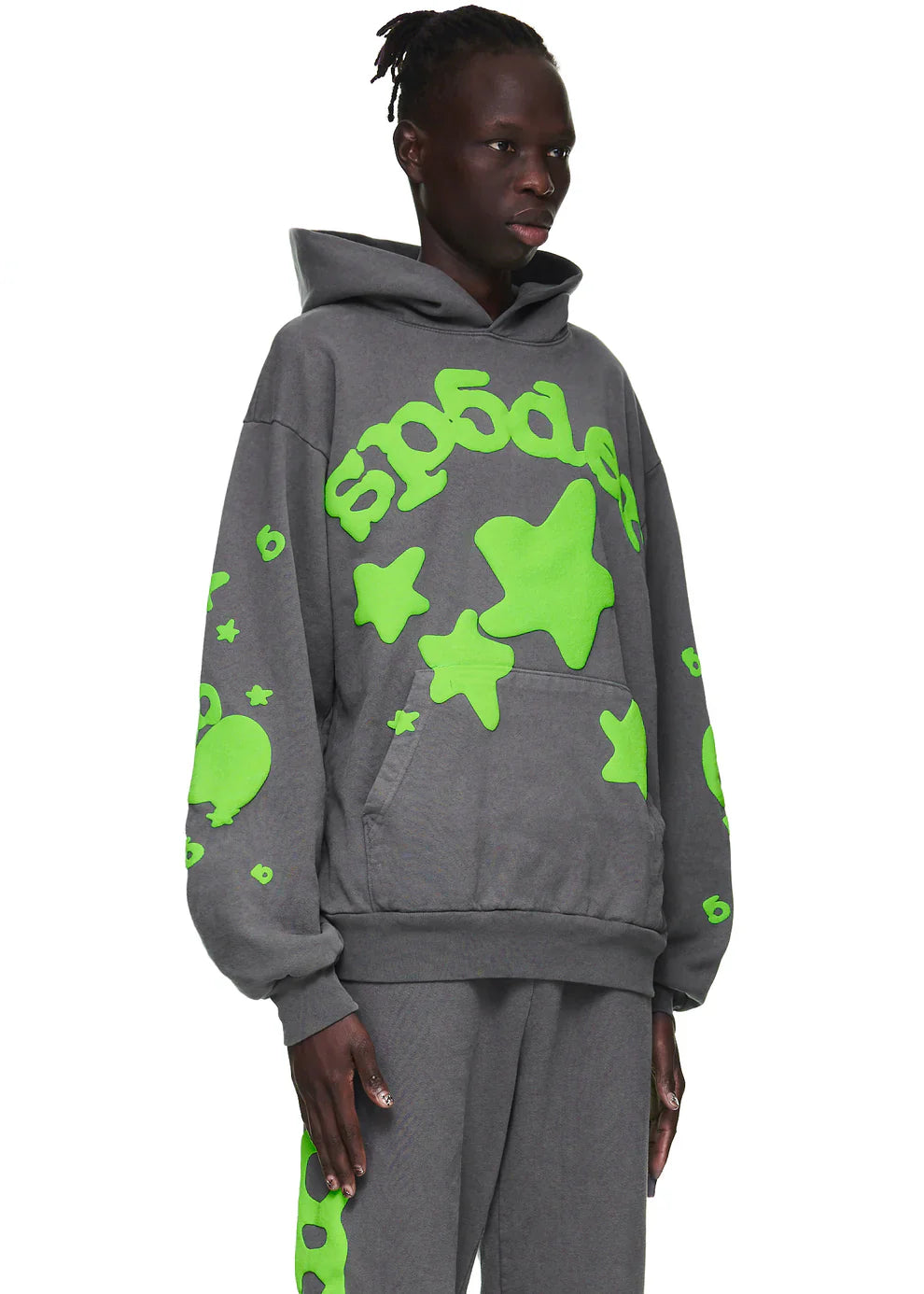 A person wears the Green and Grey Sp5der Hoodie – a 440GSM heavyweight, oversized sweatshirt with bold star graphics—standing against a plain white background for standout streetwear style.
