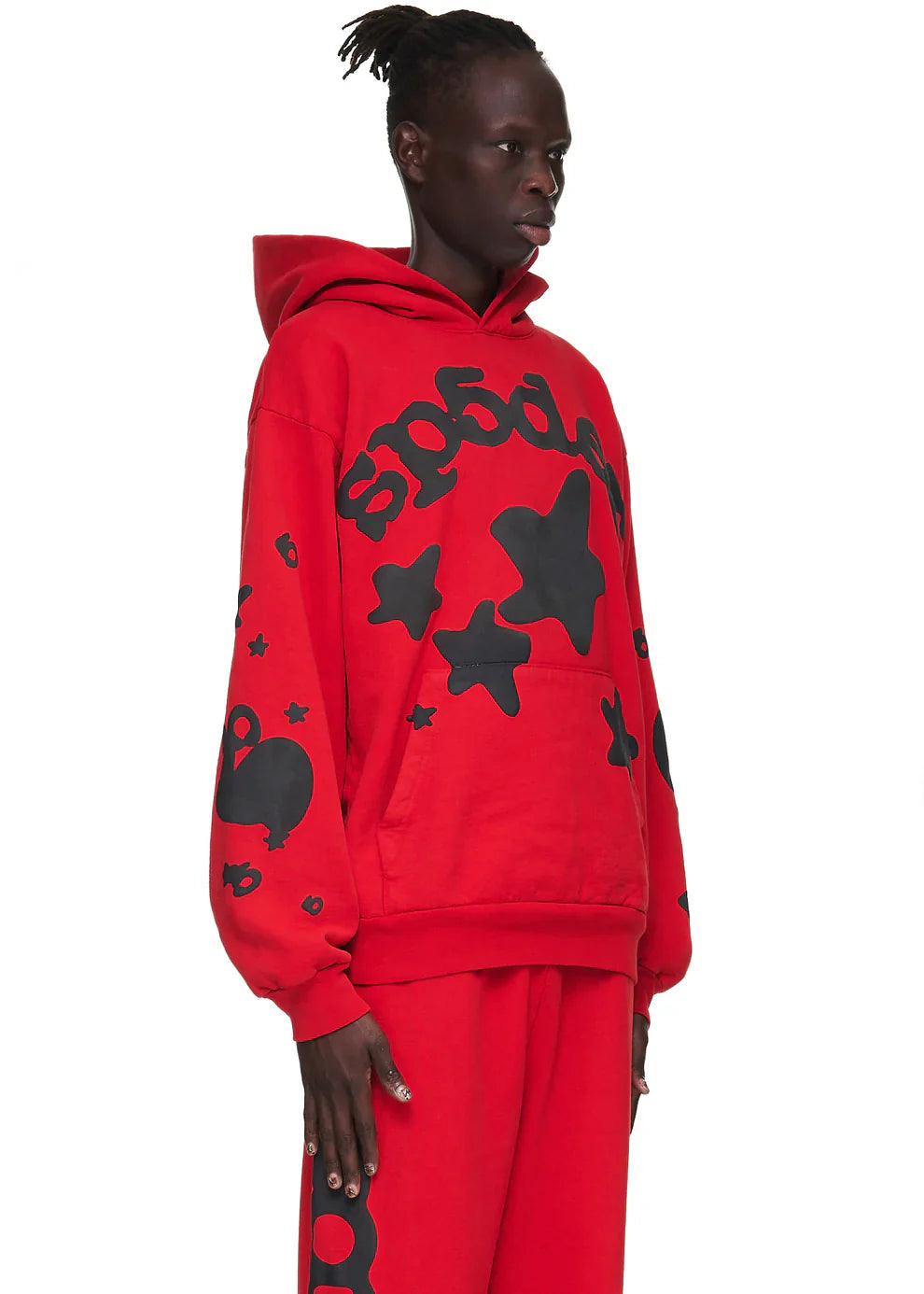 A person wears the Sp5der “Starfire” Hoodie – Red & Black 440GSM Heavyweight Oversized Streetwear Pullover and matching pants with bold star designs, standing out in a loose-fit Y2K look against a plain white background.