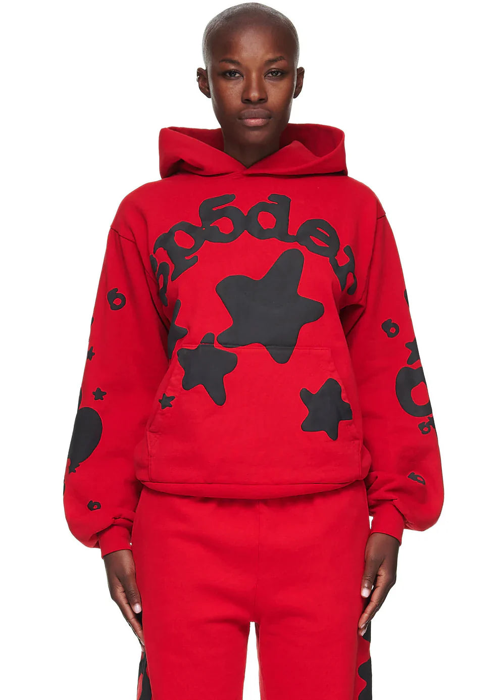 A person wears the Sp5der “Starfire” Hoodie—Red & Black 440GSM heavyweight oversized streetwear pullover—paired with matching pants, both featuring black stars and bold numbers, standing against a white background.