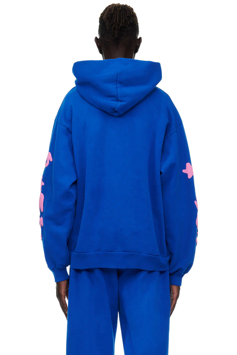A person faces away wearing the Sp5der “555 Stars” Hoodie in Royal Blue/Pink, a 440GSM heavyweight oversized streetwear pullover, paired with matching blue pants, shown against a plain white background.