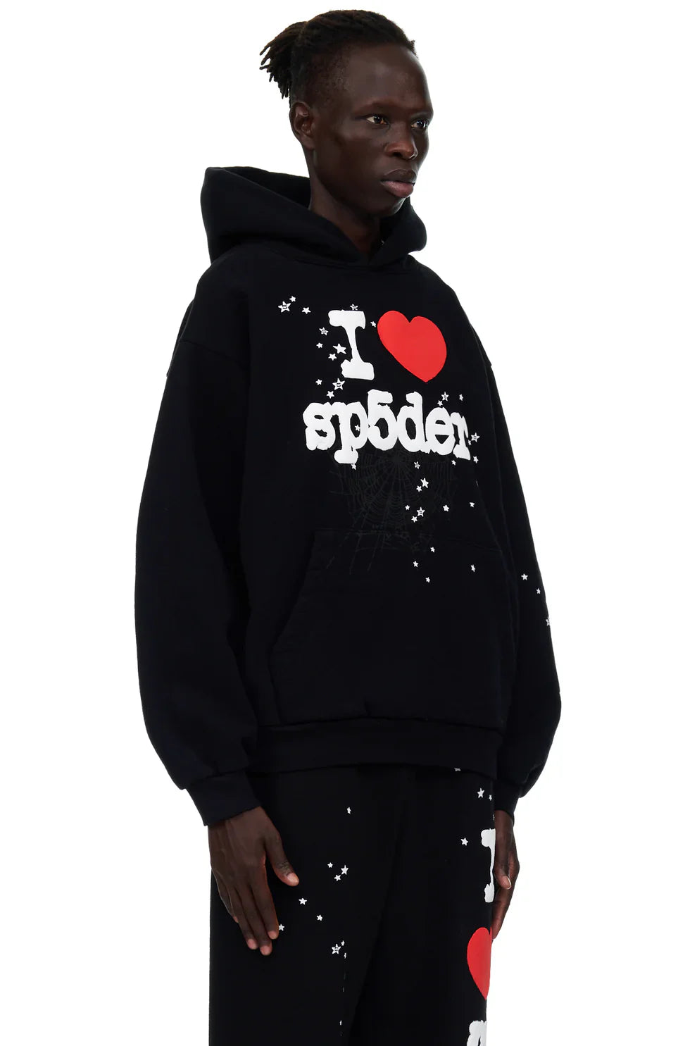 Wearing the Sp5der “I Love Sp5der” Hoodie – Black Web 440GSM Heavyweight Streetwear Pullover, paired with matching pants featuring white and red distressed text and white splatter accents, someone stands out against a white background.