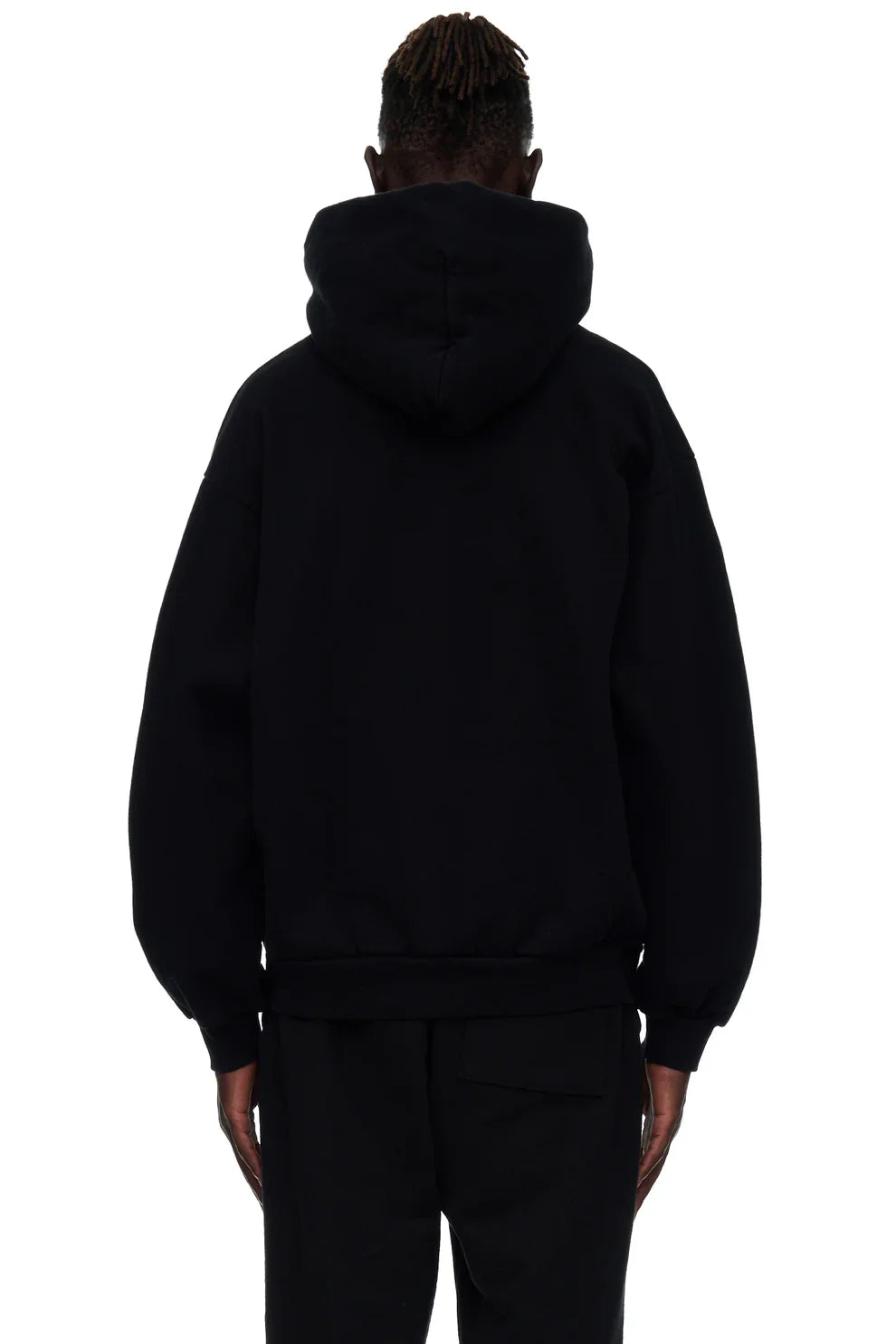 A person with short, twisted hair is shown from behind wearing the Sp5der “I Love Sp5der” Hoodie – Black Web 440GSM Heavyweight Streetwear Pullover and black pants against a white background.