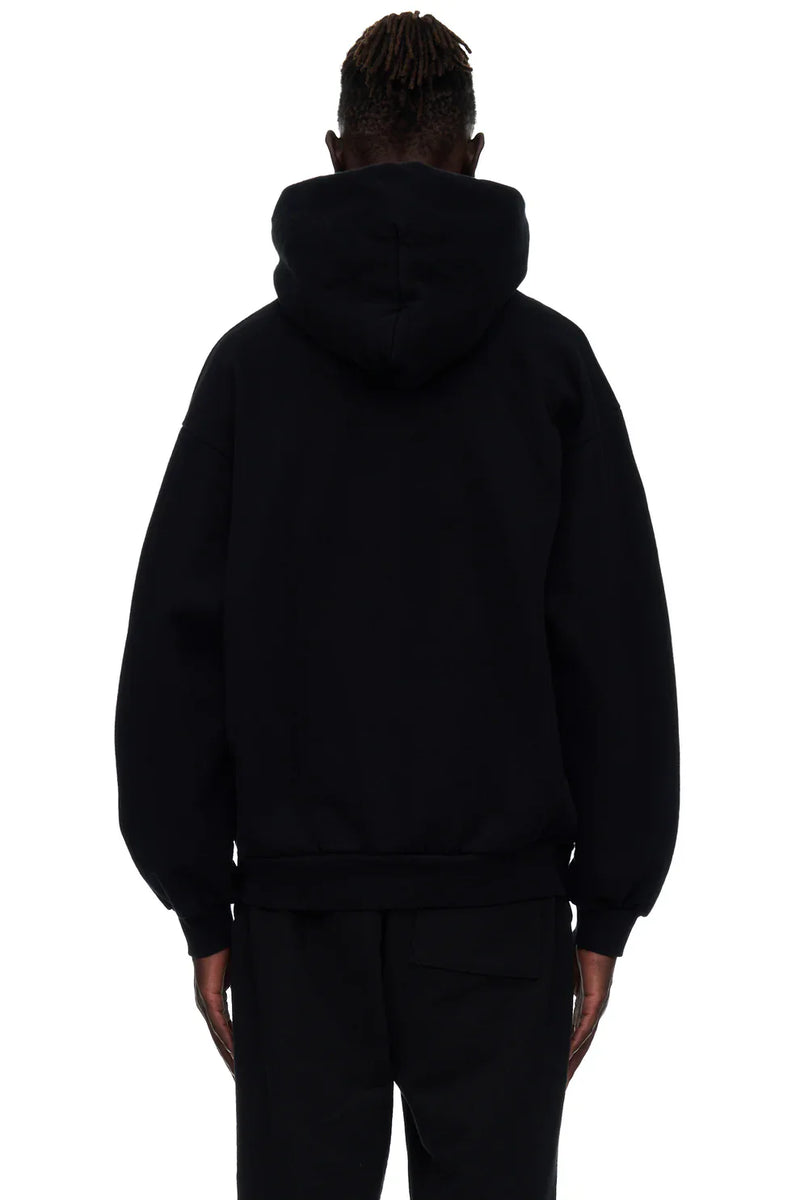 A person with short, twisted hair is shown from behind wearing the Sp5der “I Love Sp5der” Hoodie – Black Web 440GSM Heavyweight Streetwear Pullover and black pants against a white background.