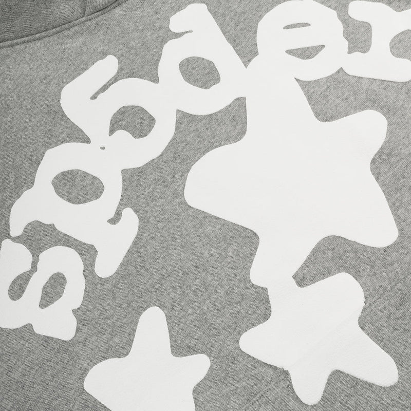 Close-up of the Sp5der Stars Hoodie – Grey 440GSM Heavyweight Streetwear Pullover, showcasing bold white text and playful abstract star shapes in a bubbly font for an eye-catching look.