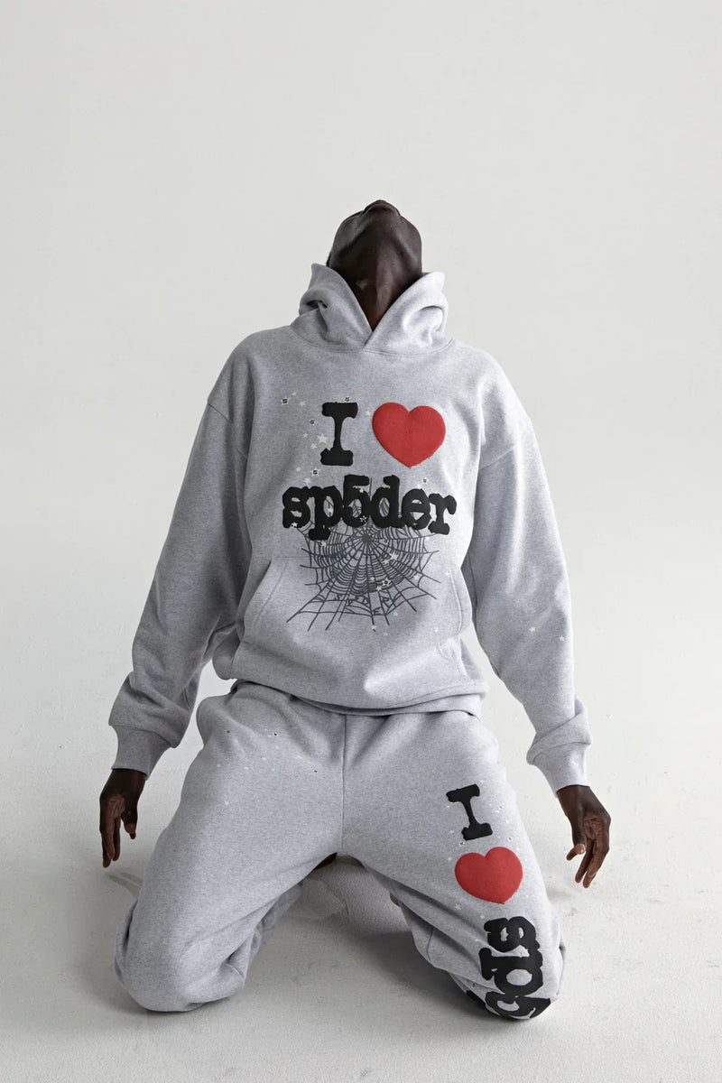 A person in a grey Sp5der “I Love Sp5der” Hoodie—440GSM heavyweight, oversized streetwear pullover—kneels and leans back against a white background, evoking Y2K style.