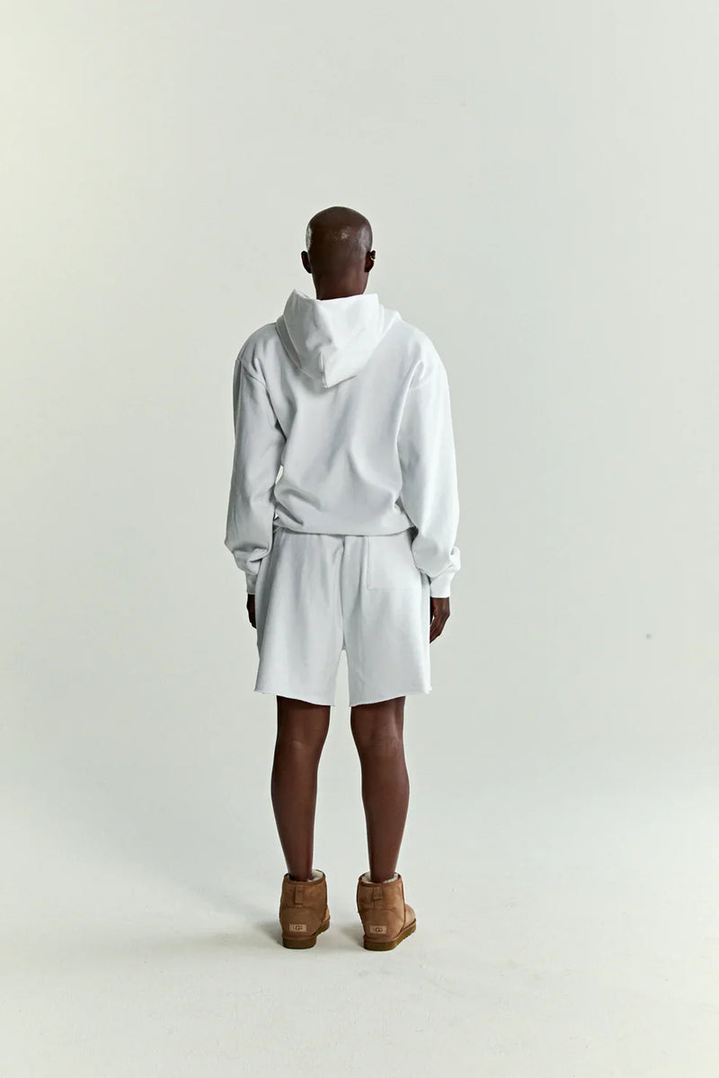 A person stands facing away in a Sp5der “Toxic Web” Hoodie – White & Neon Lime 440GSM Heavyweight Oversized Streetwear Pullover, white shorts, and tan shoes against a plain background—a cool tribute to Y2K street style.