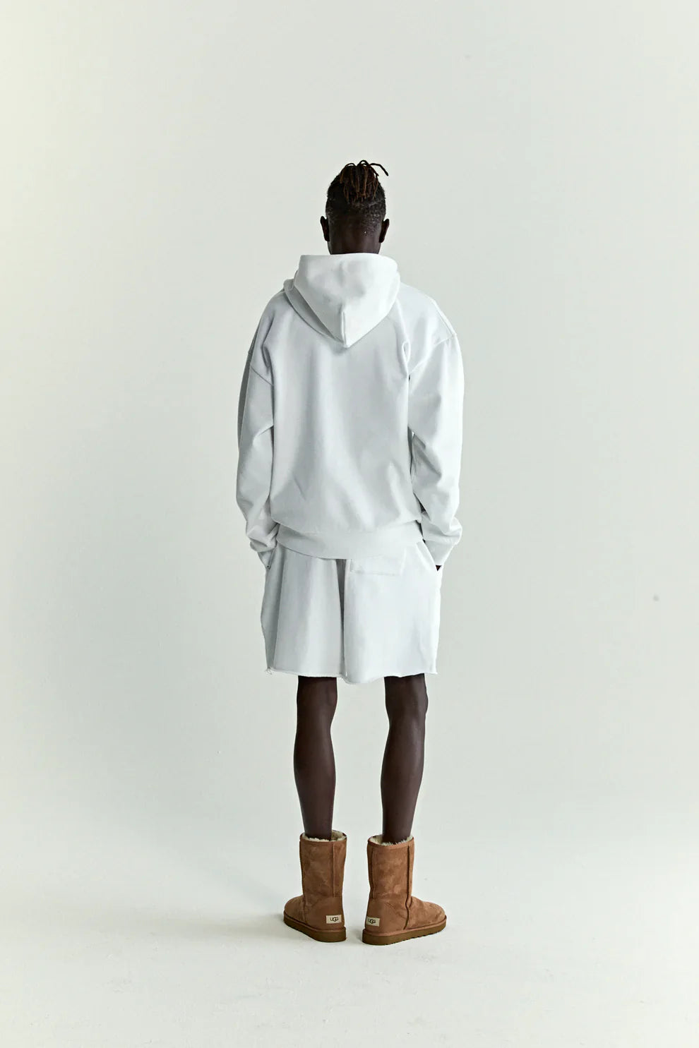 A person stands facing away wearing the Sp5der “Toxic Web” Hoodie in white & neon lime, a 440GSM heavyweight oversized streetwear pullover, paired with matching shorts and boots. Modern Y2K streetwear style against a plain light background.