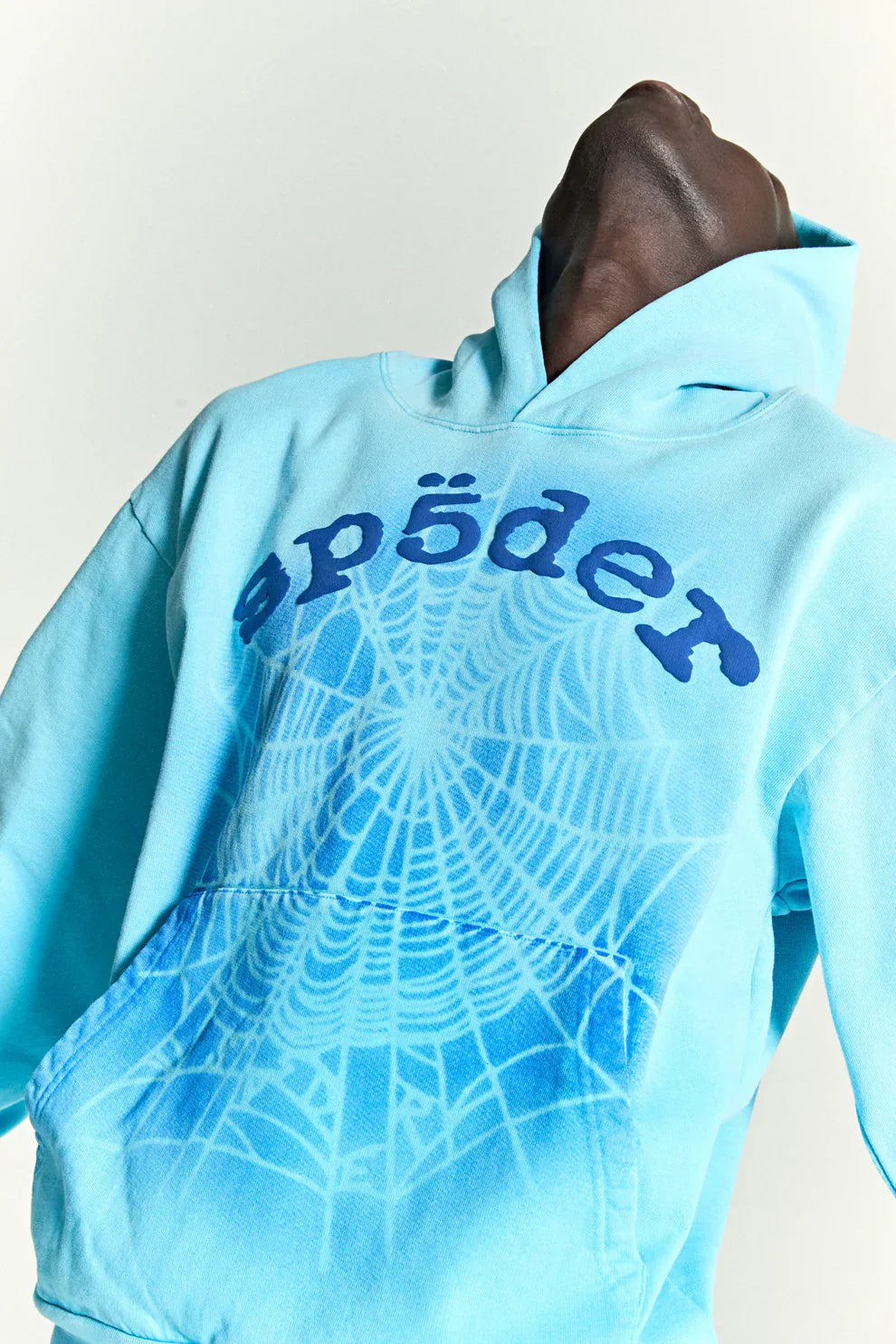 Wearing the Sp5der “Blue Venom” Web Hoodie – Sky Blue Fade, a heavyweight oversized streetwear pullover, someone leans back with their head tilted up and away from the camera.