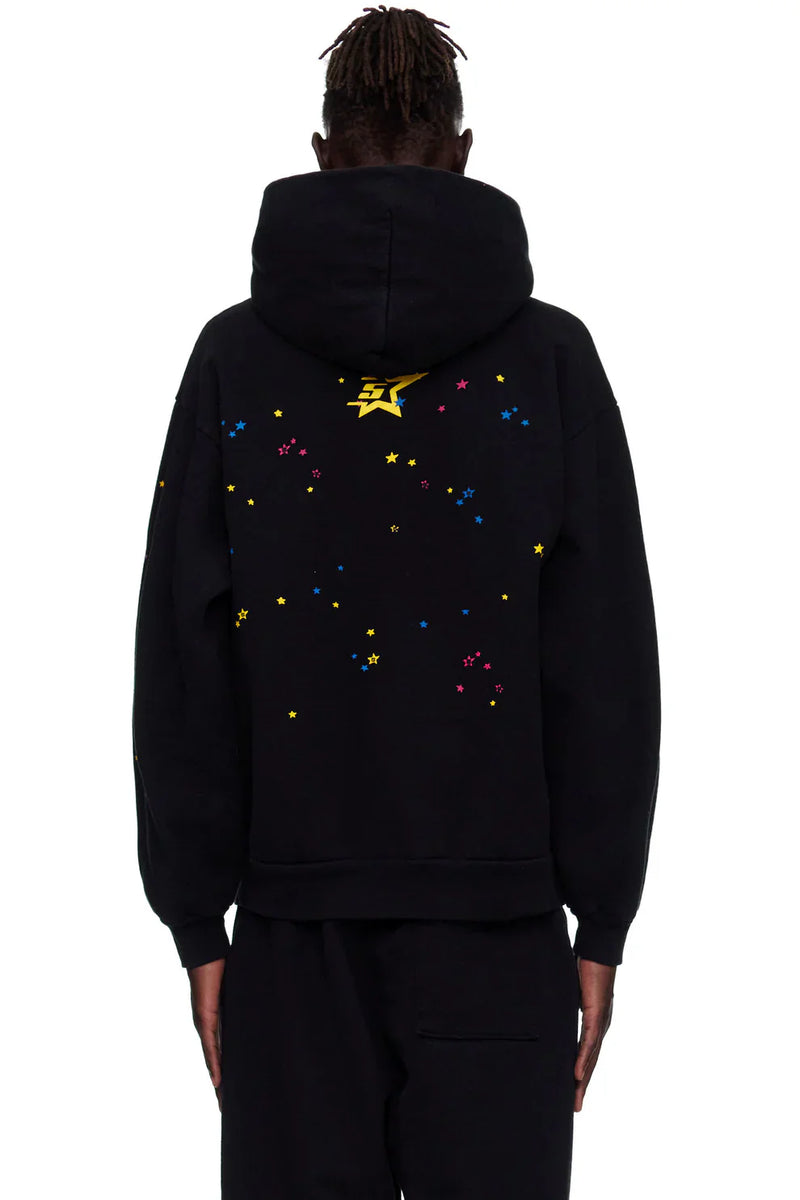 Person wearing a black Sp5der “Hares the Slime” Hoodie, a 440GSM heavyweight pullover with a spider-web streetwear design, hood up, and colorful star details including a large yellow star on the back.