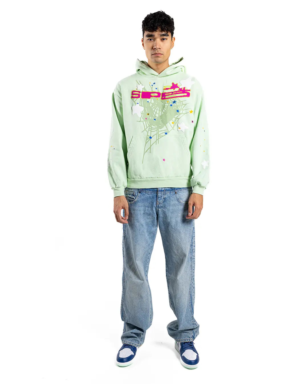 A person faces forward in a Sp5der “Mint Star Web” Hoodie – Mint Green 440GSM Heavyweight Oversized Streetwear Pullover, styled with blue jeans and blue-and-white sneakers, standing out against a crisp white background.