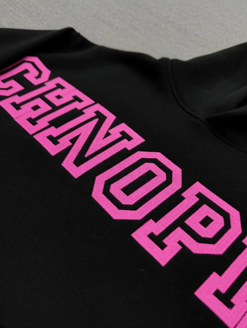 Close-up of the Sp5der Arachnophobia Black Hoodie with bold pink varsity-style lettering across the chest—a must-have streetwear piece.