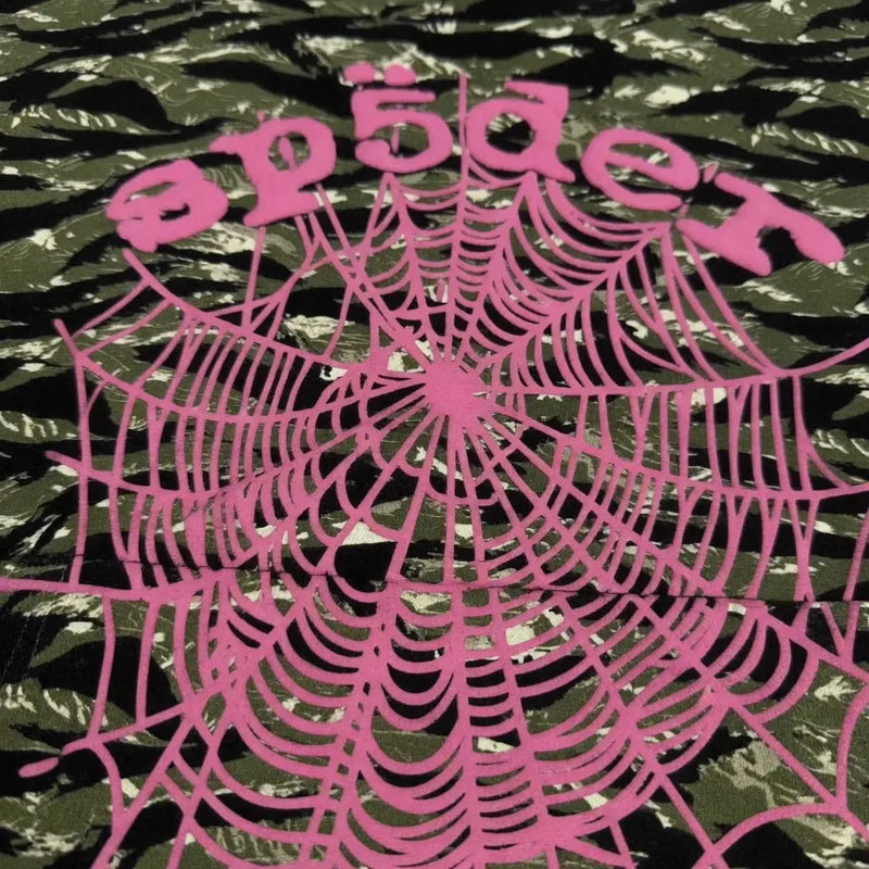 The Sp5der Tiger Camo Hoodie with Pink Spiderweb Logo features a bold pink spiderweb graphic and "Sp5der" text printed on green tiger camo fabric for a standout streetwear look.