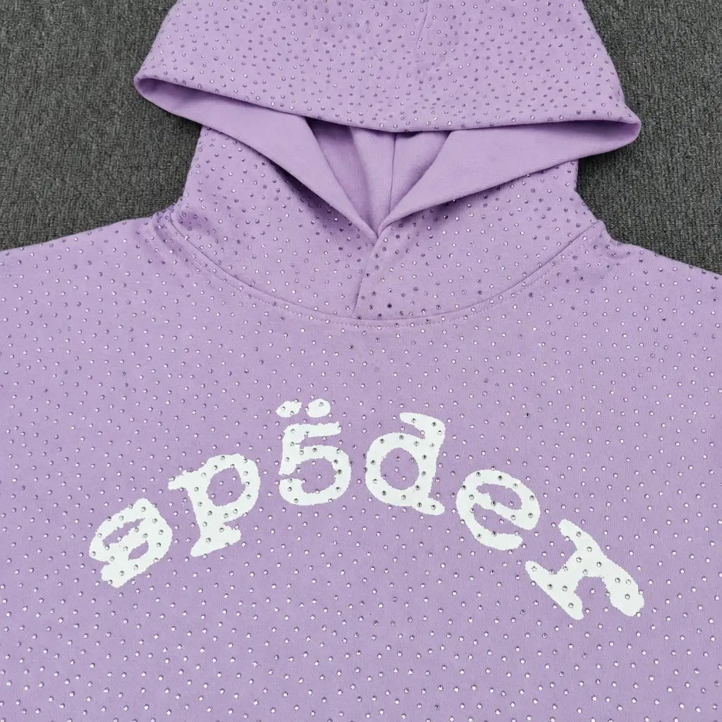 The Sp5der Rhinestone Arch Logo Light Purple Hoodie features small rhinestones and a white "sp5der" arch logo across the chest, shown on a dark gray surface—a standout streetwear essential.
