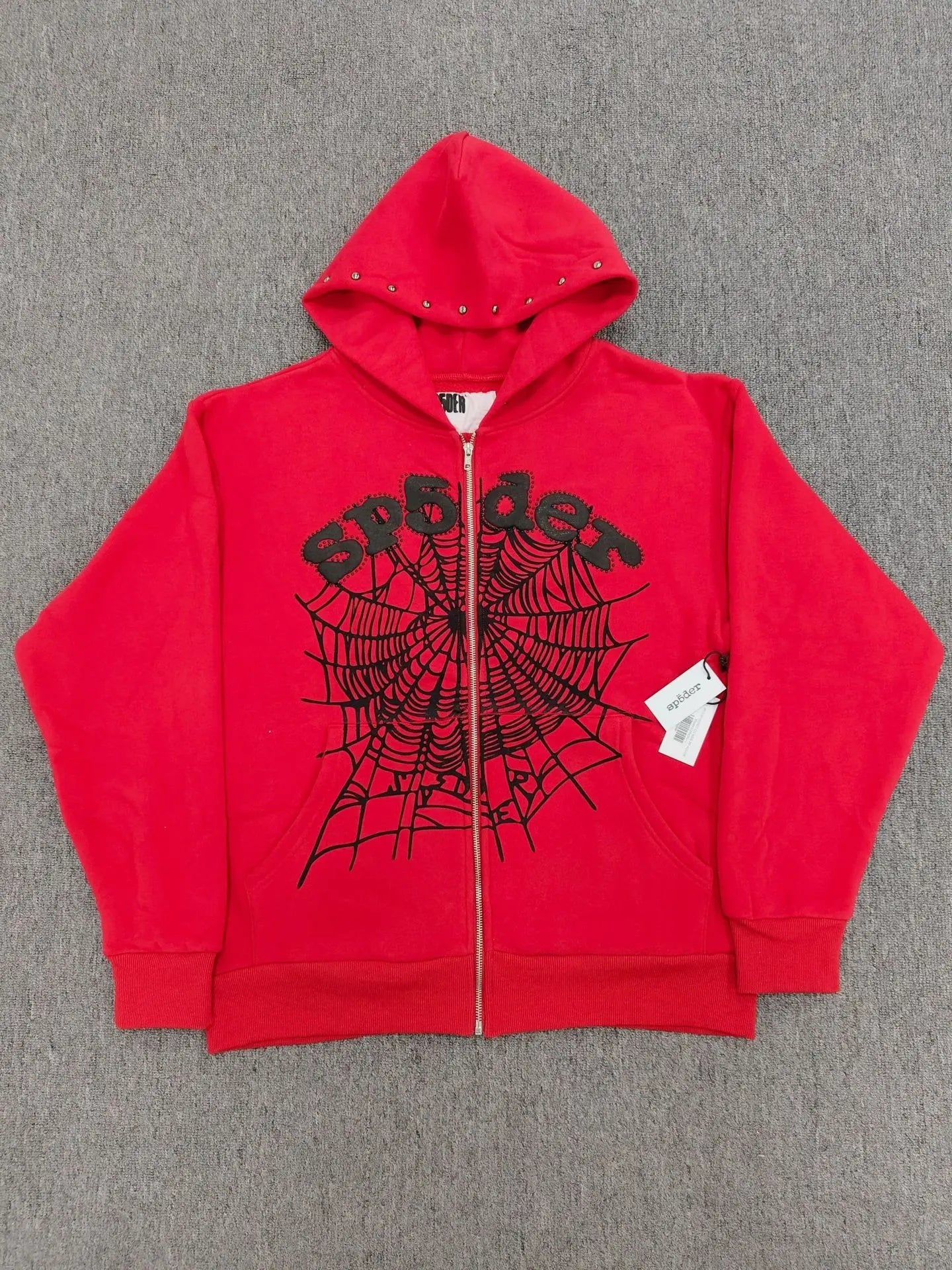 Red Sp5der zip-up hoodie with black spiderweb graphic and studded hood trim laid flat