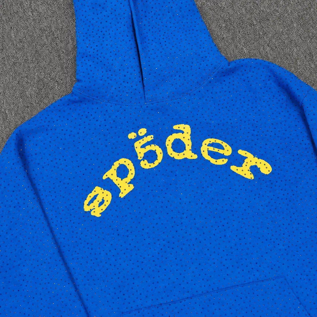The Sp5der Royal Blue Rhinestone Hoodie Yellow Arch Logo features dotted patterns and a yellow "sp5der" arch logo on the back, stylishly displayed on a gray surface.