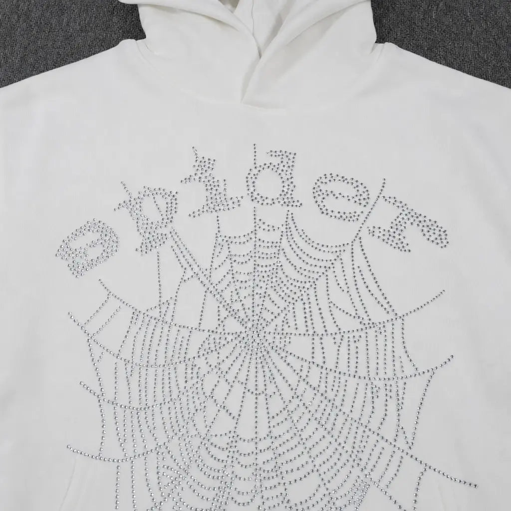 The Sp5der White Rhinestone Spiderweb Crystal Logo Hoodie is a streetwear pullover featuring "Spider" and a large crystal spiderweb design on the front, both made with shiny rhinestones.