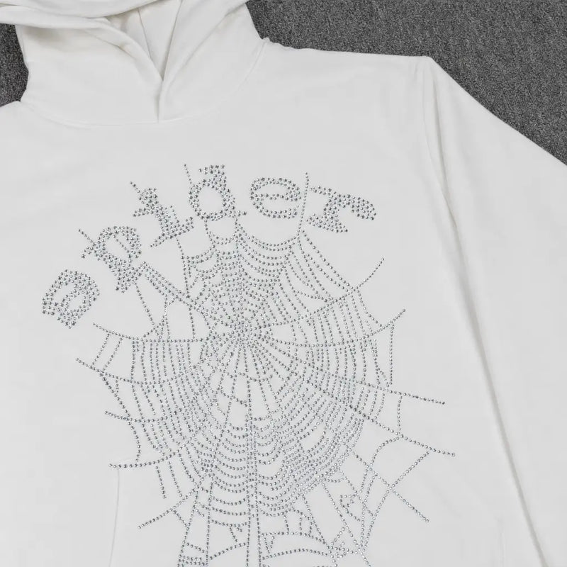 The Sp5der White Rhinestone Spiderweb Crystal Logo Hoodie features a crystal spiderweb and "spider" logo in rhinestones, laid flat on a gray surface—a bold choice for standout streetwear.