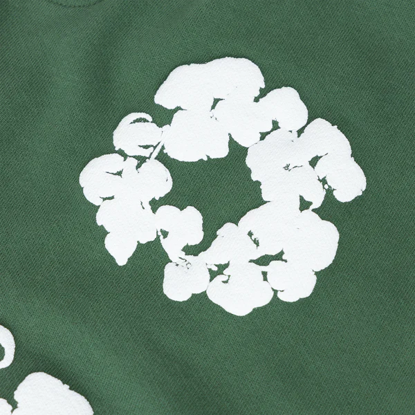 The Forest Green “Cotton Wreath” Denim Tears Sweatpants feature a white, abstract circular floral print inspired by the iconic Cotton Wreath motif, making these streetwear pants stylish and distinctive.