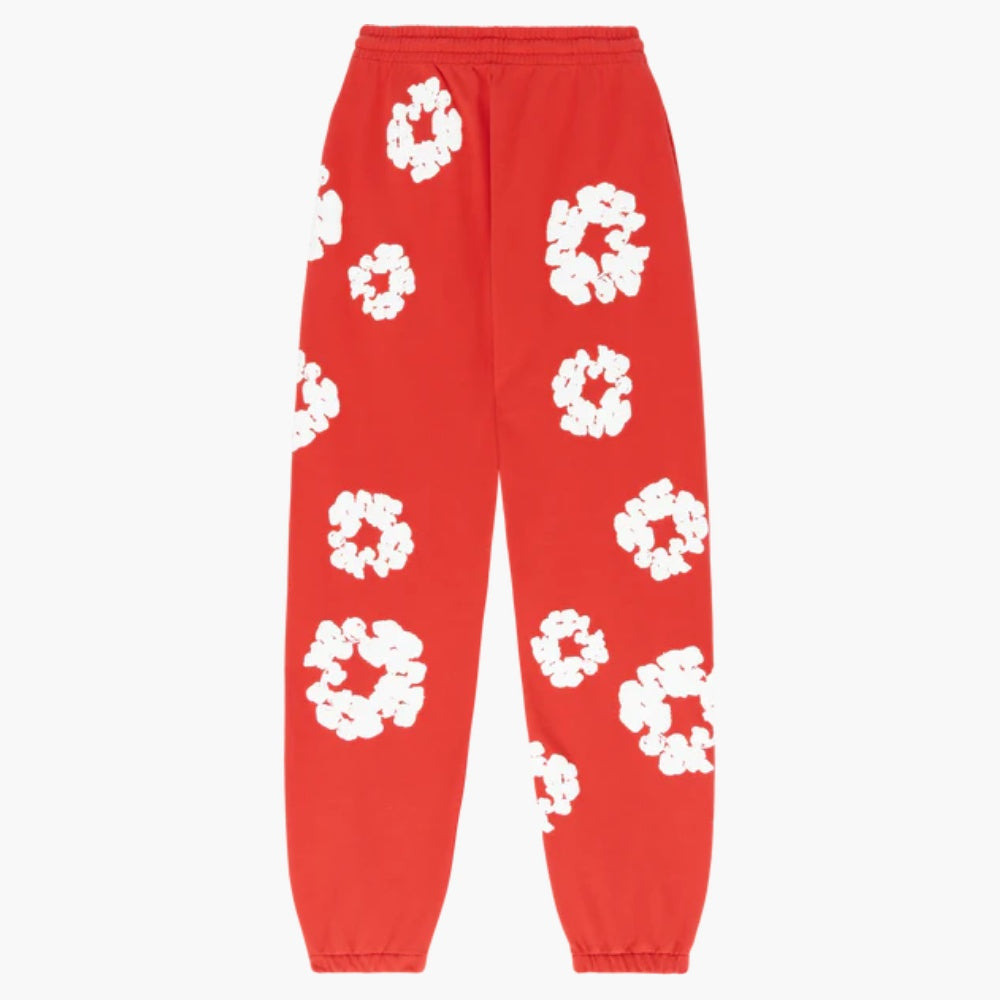 Red “Cotton Wreath” Denim Tears Sweatpants feature white floral prints on bright red fabric, finished with an elastic waistband and cuffs for comfort, embodying streetwear style.