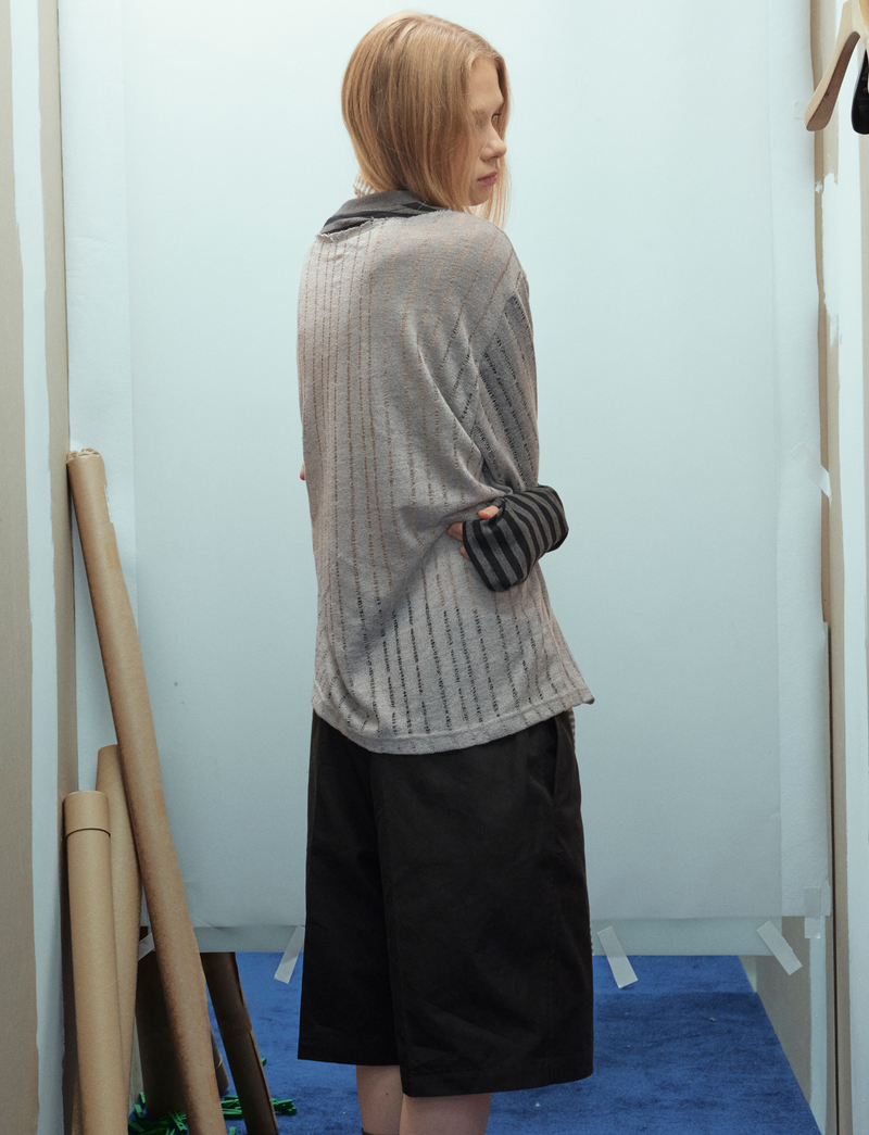 Back side view of gray sweater top with black striped sleeves on model